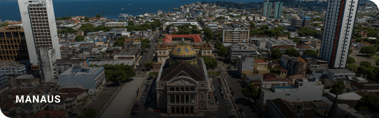 Vista aérea do centro de Manaus (AM), com destaque para o icônico Teatro Amazonas, marco histórico e cultural da capital amazonense. Ao fundo, é possível ver o encontro da arquitetura urbana com a natureza da região amazônica e o Rio Negro.
